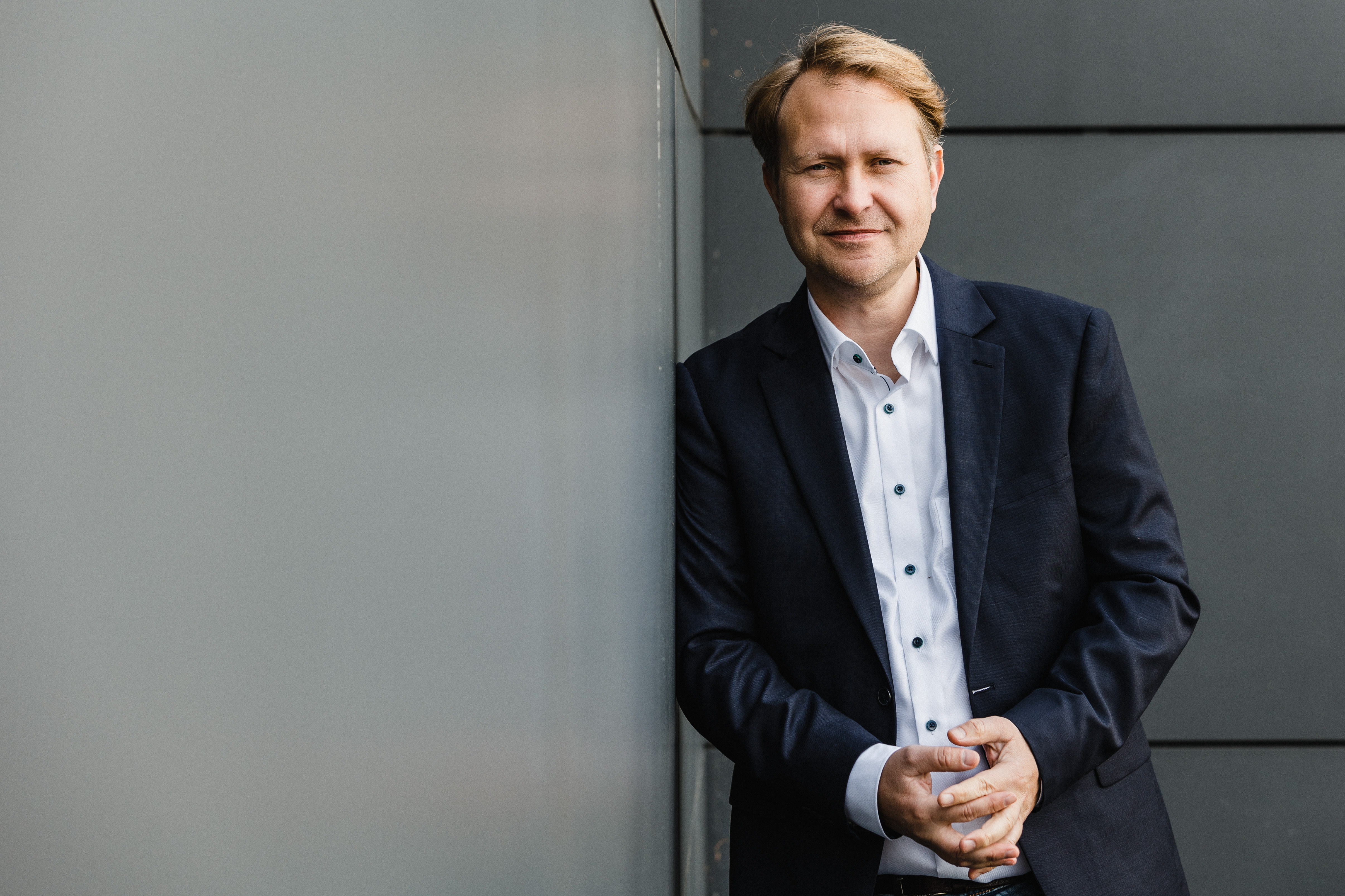 Mann in hellem Sakko vor dunkler Wand